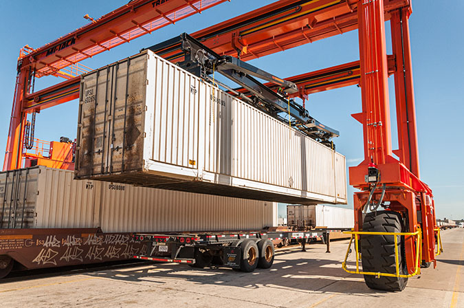 An overhead rubber tire crane moves a trailer in position.